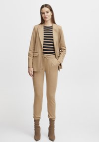 En tan blazer över en svart och tan randig topp, i kombination med tan joggers och knähöga tan stövletter, allt i mjuka tyger.