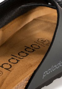 Zwarte instappersandalen met een gestructureerde bovenkant, een tan gekussen binnenzool met geprinte branding, en een stevige zwarte buitenzool.