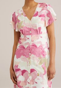 Květinové šaty s růžovými, bílými a béžovými vzory; výstřih do V, krátké volánkové rukávy a zapínání na knoflíky vpředu. Měkká textilie.