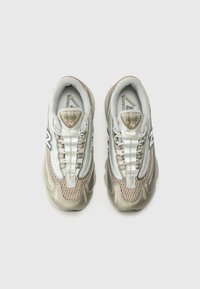 Baskets New Balance 1000, avec une tige en mesh beige et argent, une semelle texturée, des lacets bien visibles et un logo sur le côté.