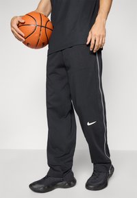 Melnas basketbola bikses no mīksta auduma, ar sānu baltu svītru un mazu baltu Nike logotipu. Apvienotas ar melniem sporta apaviem.