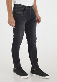 Schmale schwarze Jeans aus Denim mit einer verblassten Textur, Five-Pocket-Design und einer engen Passform, kombiniert mit schwarzen Sneakers.