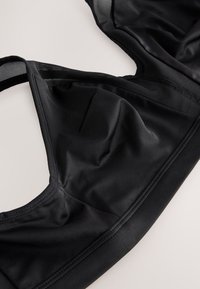 Zwarte sportbeha met glad, rekbaar materiaal, naadloos ontwerp en mesh panelen voor ademend vermogen. Platte naden voor comfort.