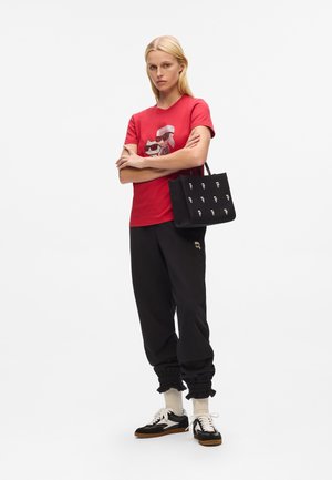 Red graphic t-shirt, black joggers with elastic cuffs, black tote bag with white pattern, and black and white sneakers with gum soles.