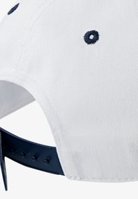 Hvid bomuldsbaseballkappe med marineblå stikninger og en justerbar plastikrem på bagsiden, samt ventilationshuller på toppen.