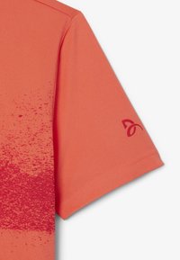 Korallfärgad kortärmad skjorta med ett gradientmönster som övergår från enfärgad till prickig röd, med en märkeslogotyp på ärmen.