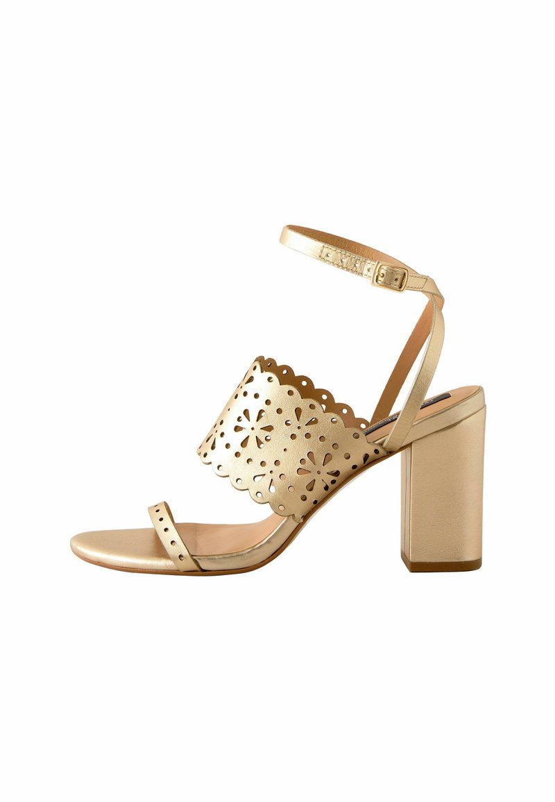 Gold heeled sandal with an open toe design, scalloped cutouts, and a wide strap. Features an ankle strap and a chunky block heel.