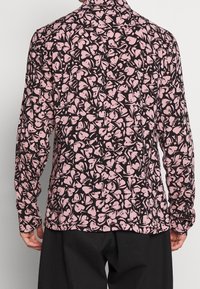 Långärmad skjorta i mörkt tyg med ett rosa abstrakt hjärtmönster, har krage och knappmanchetter. Mjuk textur.