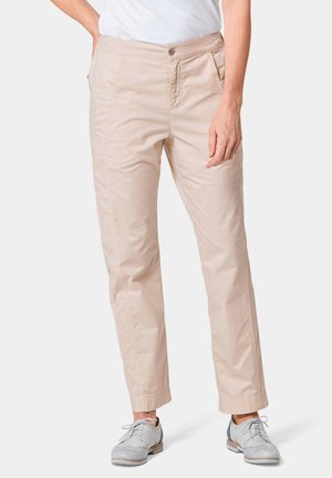 Pantaloni in cotone beige con design a gamba dritta, tasche frontali e chiusura a bottone. Texture liscia con dettagli minimi. Indossati con scarpe grigie.