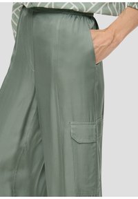 Ljust gröna satinbyxor med elastisk midja, sidofickor och en cargoficka, med en slät och glänsande textur.