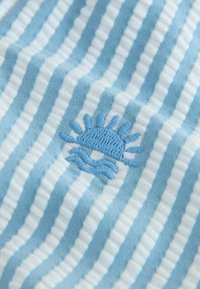 Diseño de sol azul claro bordado en tela blanca con rayas azules, que presenta una textura suave y rayas alternadas.