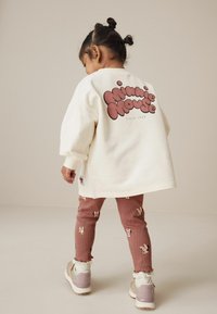 Kreemist oversized sviitriga, mille seljal on "Minnie Mouse" graafika, koos roosa ribakujulise voodriga retuusidega, millel on jänese muster ja volangidega varrukad.