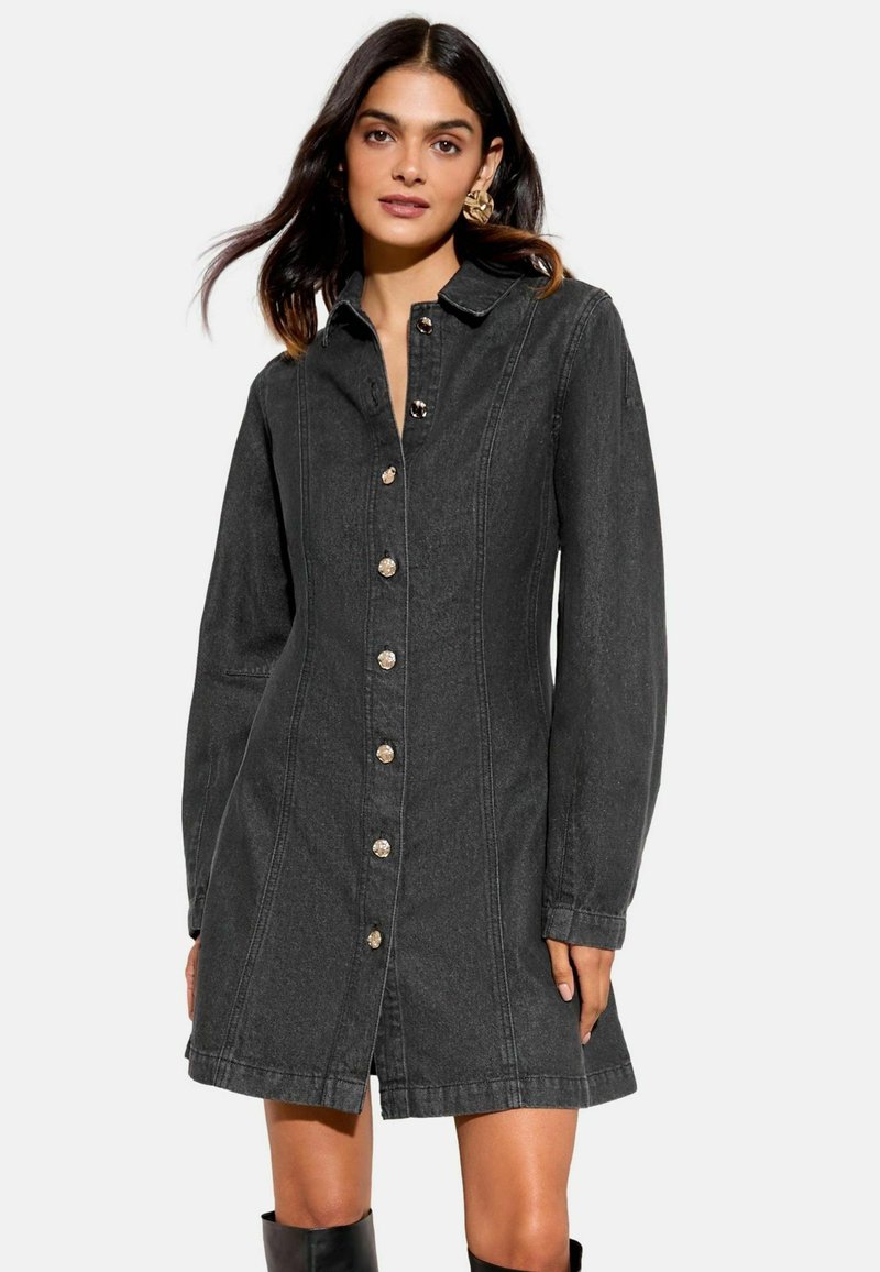 Musta farkkutunika pitkillä hihoilla, napit edessä ja rakennettu kaulus. Sisältää näkyvää ompelua ja kevyen rakenteen.