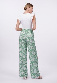 Blusa blanca con mangas acampanadas combinada con pantalones anchos de flores verdes. Presenta cintura elástica y tejido ligero con un patrón de hojas tropicales.