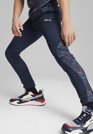 Navy athletic pants with red wave pattern accents, featuring a small logo, paired with multicolored athletic shoes and black socks.
