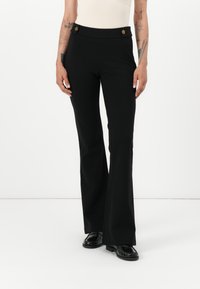 Pantaloni neri a zampa d'elefante realizzati in tessuto elasticizzato, con vita alta, due bottoni frontali e una texture morbida. Abbinati a scarpe nere.