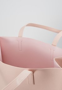 Lichtroze tote bag met een gestructureerde buitenkant en een gladde binnenkant. Beschikt over twee handvatten en gestikte details langs de randen.