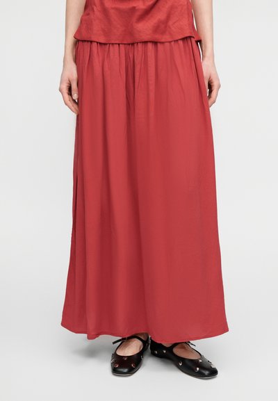 Κόκκινη, ρέουσα μάξι φούστα από ελαφρύ ύφασμα, με ελαστική μέση και ομαλή υφή. Συνδυασμένη με μαύρα παπούτσια.