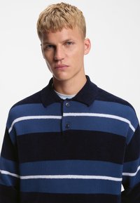 Navy and blue striped knit polo shirt features a classic collar and two-button placket, with soft texture and varying stripe widths.
