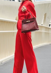 Röd ribbad tröja tillsammans med vida röda byxor. Bär en mörkröd handväska med krokodilpräglat mönster och detaljer i guld.