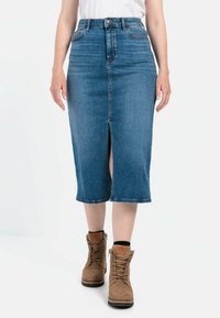 Mellemlang denimnederdel i mørkeblå med en forslid, med en høj talje, tonalt syning og rå kant. Båret med brune snøresko.
