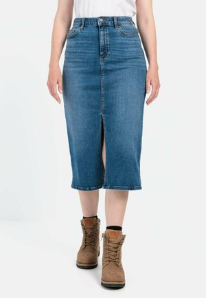 Mid-length denim skirt in dark blue with a front slit, featuring a high waist design, tonal stitching, and a raw hem. Worn with brown lace-up boots.
