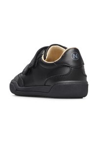 Scarpa bassa nera con fasce in velcro, rivestimento interno beige e logo "N" sul tallone, vista dalla parte posteriore su sfondo bianco.