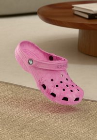 Rosa Crocs mit Belüftungsöffnungen, glatter Textur und schwarzem Logo-Akzent. Leichtes Design mit einem Riemen für einen sicheren Sitz.