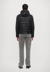 Chaqueta acolchada negra con capucha, con un diseño acolchado y tela lisa, combinada con pantalones rectos gris, vista desde la parte posterior.