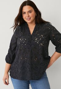 Camicia nera ricamata con motivi floreali, maniche a sbuffo a tre quarti, scollatura a V e dettagli con bottoni. Tessuto morbido e strutturato.