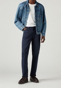 Jeansjacka med ljus tvätt, bröstficka, vit t-shirt, marinblå chinos och bruna snörskor. Enkel design, avslappnad passform, minimal detaljering.