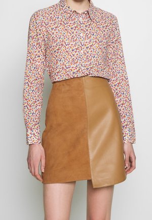 Mujer con camisa de manga larga estampada con flores y falda corta de cuero y ante marrón de dos tonos.