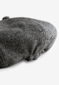 Grå ullberet med en strukturerad yta, rund form och en knappdetalj på toppen. Tyget har ett mjukt, något ludet utseende.