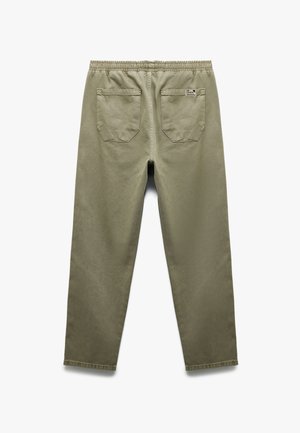 Olijfgroene broek met een gladde textuur, elastische tailleband en twee achterzakken met een patch, voorzien van hoekige ontwerpen en een klein label.