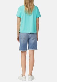 T-shirt di cotone azzurro chiaro con maniche corte abbinato a pantaloni corti in denim con orlo arrotolato. Sneaker bianche completano l'outfit.
