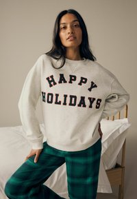 Ljusgrå sweatshirt med "GLADA HÖGTIDER" i fet röd och mörkgrön text, ihop med gröna rutiga byxor. Mjuk tyg och avslappnad passform.