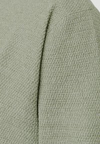 Tissu de pull en maille texturé vert clair avec un motif tricoté. Le matériau est doux et légèrement extensible, présentant une surface lisse et uniforme.