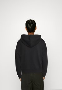 Sudadera negra de gran tamaño con un bolsillo canguro y capucha con cordón, hecha de algodón suave, con puños y dobladillo acanalados.
