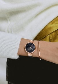 Montre en or rose avec un bracelet en tissu noir, dotée d'un cadran sombre et de fines index horaires. Accompagnée d'un fin bracelet en or rose.