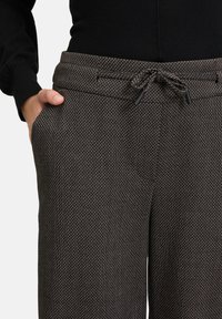 Gewebte Schwarz- und Weiß gemusterte Hose mit elastischem Bund, seitlichen Taschen und einer lockeren Passform, die subtile Texturdetails hervorhebt.