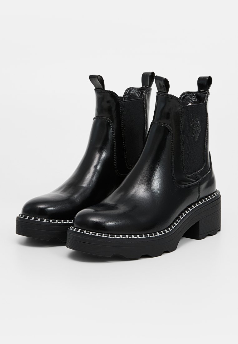Bottines Chelsea en cuir noir avec des accents élastiques sur les côtés, présentant un talon épais et des coutures blanches contrastantes le long de la semelle.