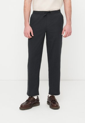 Pantalon gris foncé à cordon de serrage avec une coupe décontractée, en tissu texturé, accompagné de chaussures marron à lacets. Design minimaliste, sans motifs visibles.