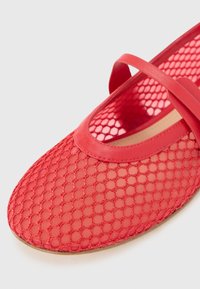 Bailarinas de malla rojas con un patrón texturizado de panal. Presentan una punta suave y redondeada y una tira delgada en la parte superior.