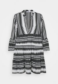 Svart och vit mönstrad klänning med geometriska former, V-ringning, trekvartsärmar och en rynkad nederkant.