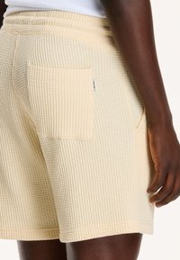 Waffle-textured, light yellow shorts with a back pocket and an elastic waistband; soft, breathable fabric with subtle stitching details.