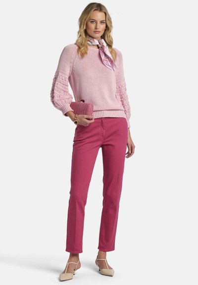 Suéter de punto rosa con mangas texturizadas, combinado con pantalones fucsia. Complementado con un bolso de mano rosa y zapatos de tacón de color claro.