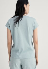 Světle modré tričko s krátkým rukávem a volným střihem, vyrobené z měkké bavlny. Zadní část má jednoduchý, bezproblémový design.