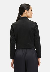 Zwarte cropped jas met een zachte textuur, voorzien van een kraag en lange mouwen. De achterkant heeft minimaal stikwerk en een getailleerd ontwerp.