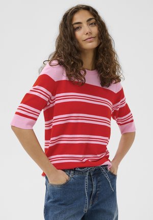 Punaste ja roosade triipudega lühikeste varrukatega kampsun, soonikkoes kaelus ja lõdva istuvusega. Sobitatud siniste teksadega.