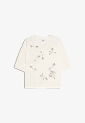 Biela krátkym rukávom košeľa s rôznymi striebornými bezpečnostnými špendlíkmi pripevnenými a rozptýlenými po prednej strane.